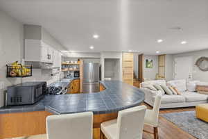 Kitchen featuring black microwave, open shelves, freestanding refrigerator, a peninsula, and recessed lighting