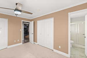Unfurnished bedroom featuring an office area, ornamental molding, a ceiling fan, light colored carpet, and a closet