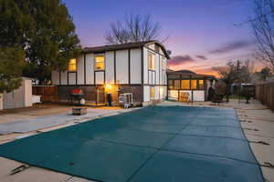 Back of house at dusk featuring a fenced backyard, a patio area, brick siding, a sunroom, and stucco siding