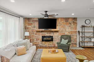 Living room featuring a stone fireplace, wood finished floors, ceiling fan, and recessed lighting