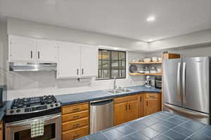 Kitchen featuring stainless steel appliances, open shelves, under cabinet range hood, tile countertops, and recessed lighting