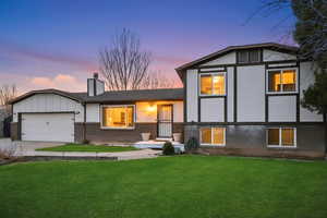 Tri-level home with a lawn, brick siding, concrete driveway, and a chimney