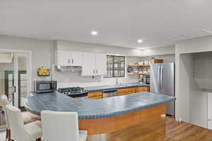 Kitchen with appliances with stainless steel finishes, open shelves, a kitchen bar, a peninsula, and tile countertops