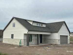 View of front of house featuring stone siding, stucco siding, roof with shingles, and an attached garage