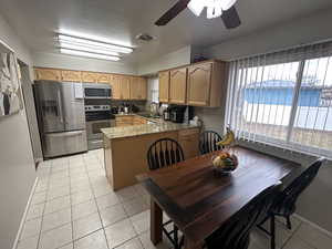Kitchen featuring appliances with stainless steel finishes, light stone countertops, light tile patterned floors, a peninsula, and a ceiling fan