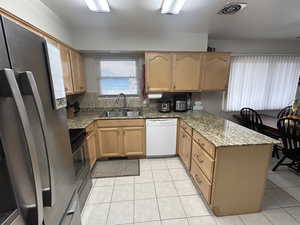 Kitchen featuring appliances with stainless steel finishes, light stone counters, a peninsula, and light tile patterned floors