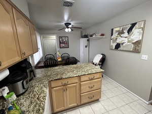 Kitchen featuring a peninsula, light stone countertops, ceiling fan, and light tile patterned floors