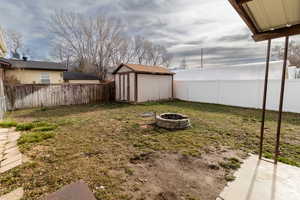 Fenced backyard featuring a fire pit and a storage unit