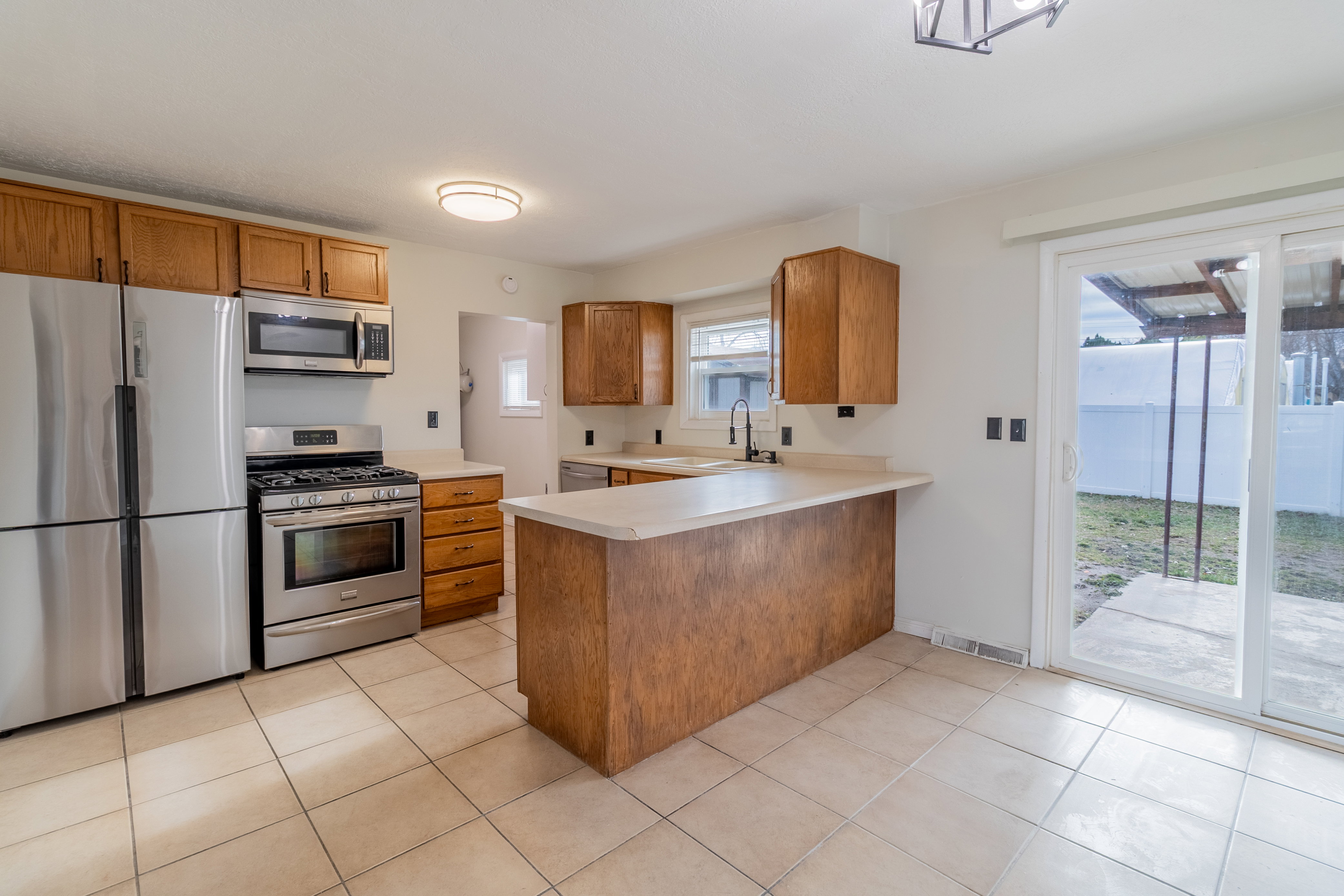 Kitchen with stainless steel appliances, light countertops, a peninsula, brown cabinetry, and light tile patterned flooring