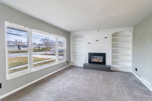 Unfurnished living room with built in shelves, a brick fireplace, light colored carpet, and a textured ceiling