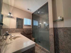 Bathroom with vanity, a shower stall, tile walls, and a wainscoted wall