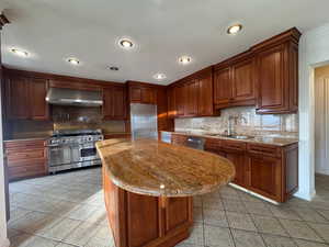 Kitchen featuring light stone counters, high end appliances, wall chimney range hood, light tile patterned flooring, and recessed lighting