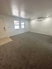Empty room featuring a textured ceiling, light colored carpet, and a wall unit AC