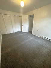 Unfurnished bedroom featuring two closets, a textured ceiling, a baseboard radiator, and dark carpet