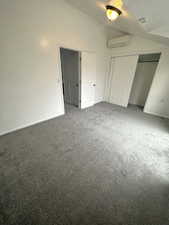 Unfurnished bedroom featuring carpet, a textured ceiling, a wall mounted AC, a closet, and high vaulted ceiling