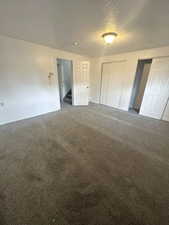 Unfurnished bedroom with dark colored carpet, a textured ceiling, and two closets
