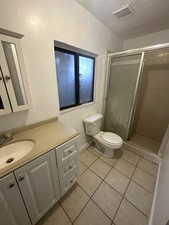 Full bath featuring vanity, a shower stall, a textured ceiling, and light tile patterned floors