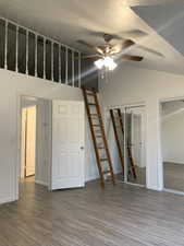Unfurnished bedroom featuring vaulted ceiling, dark wood-style floors, multiple closets, a ceiling fan, and a textured ceiling