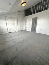 Unfurnished bedroom featuring vaulted ceiling, two closets, a textured ceiling, carpet floors, and a wall mounted air conditioner