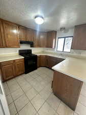Kitchen featuring light countertops, black electric range oven, a textured ceiling, a peninsula, and light tile patterned floors