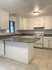 Kitchen featuring dark countertops, white range with electric cooktop, white cabinetry, a textured ceiling, and a peninsula