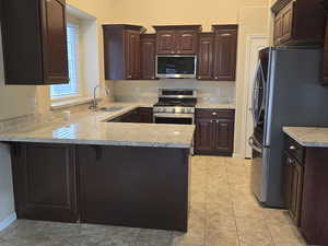 Kitchen featuring dark wood finish cabinetry, a peninsula, stainless steel appliances, and a kitchen bar