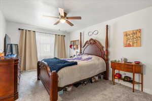 Bedroom with light colored carpet, ceiling fan, and a textured ceiling