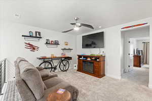 Living area with ceiling fan, light carpet, a glass covered fireplace, and a textured ceiling