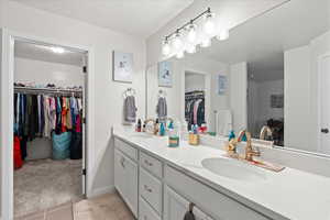 Bathroom featuring a spacious closet, double vanity, a textured ceiling, and light carpet