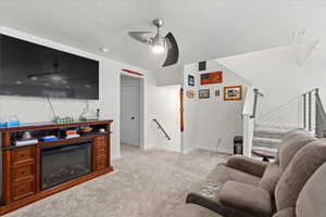 Living room with ceiling fan, light colored carpet, stairway, a textured ceiling, and a glass covered fireplace