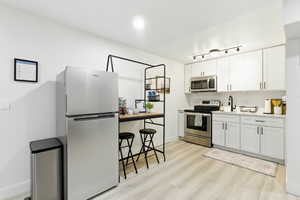 Kitchen with appliances with stainless steel finishes, light countertops, white cabinetry, and light wood finished floors