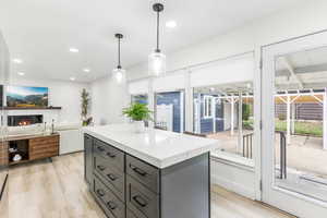 Kitchen with a warm lit fireplace, a kitchen island, gray cabinets, hanging light fixtures, and light wood-type flooring