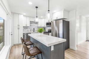 Kitchen with appliances with stainless steel finishes, white cabinetry, decorative light fixtures, a kitchen breakfast bar, and a kitchen island