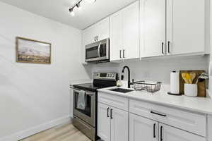 Kitchen featuring appliances with stainless steel finishes, white cabinetry, light wood-style floors, track lighting, and light stone counters
