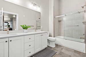 Bathroom featuring double vanity and bath / shower combo with glass door