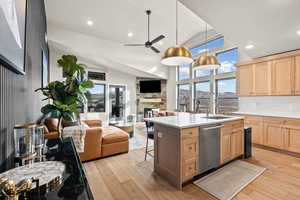 Kitchen featuring open floor plan, light brown cabinets, a fireplace, a ceiling fan, and high vaulted ceiling