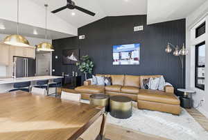Living room with light wood-style floors, lofted ceiling, an accent wall, ceiling fan, and recessed lighting