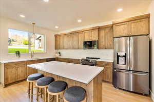 Kitchen featuring stainless steel appliances, decorative backsplash, light wood-style flooring, and a kitchen bar