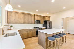 Kitchen featuring stainless steel appliances, light wood finished floors, a kitchen bar, a center island, and wood finish cabinets