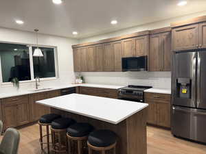 Kitchen with black appliances, a kitchen island, a kitchen bar, hanging light fixtures, and tasteful backsplash
