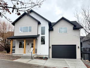 View of front of house with board and batten siding, a porch, a garage, driveway, and roof with shingles