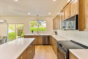 Kitchen with stainless steel appliances, light wood-type flooring, tasteful backsplash, wood finish cabinetry, and light stone counters