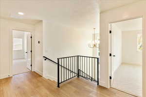 Hall with an upstairs landing, light wood-style floors, a textured ceiling, and suspended lighting
