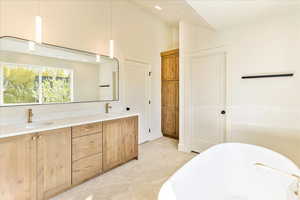 Full bath with double vanity, a freestanding tub, lofted ceiling, light flooring, and recessed lighting
