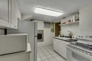Kitchen with white appliances, white cabinetry, open shelves, light tile patterned floors, and a textured ceiling