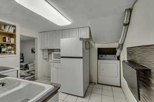 Kitchen featuring white cabinets, washer / dryer, white appliances, and light tile patterned flooring