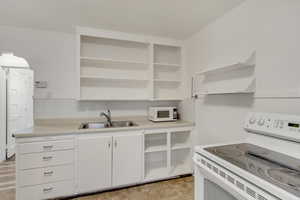 Kitchen with open shelves, white appliances, white cabinetry, and light countertops