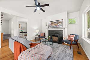 Living area featuring stairs, a tile fireplace, light wood-style flooring, and a ceiling fan