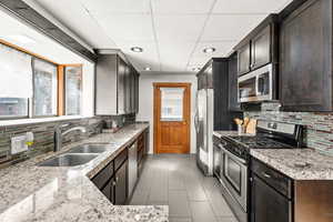 Kitchen with stainless steel appliances, tasteful backsplash, a paneled ceiling, light stone countertops, and recessed lighting