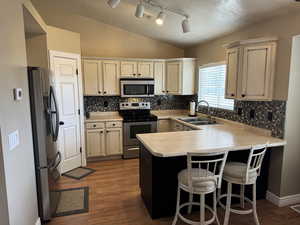 Kitchen featuring light countertops, stainless steel appliances, a peninsula, vaulted ceiling, and a kitchen breakfast bar